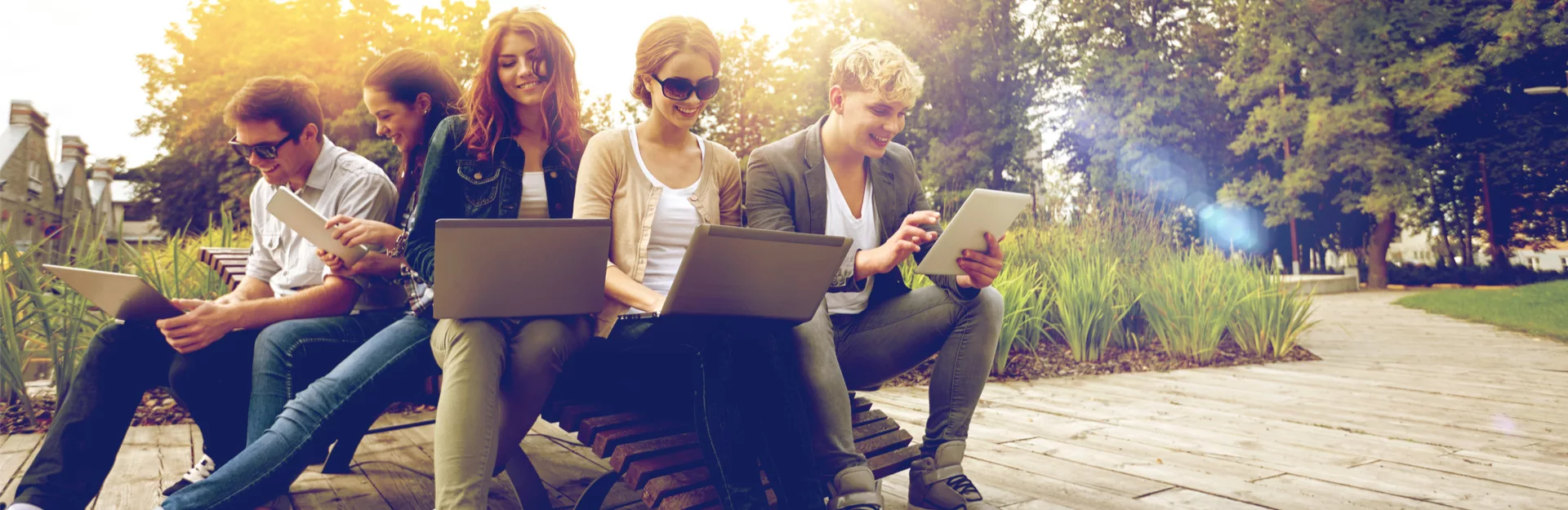 Jugendliche sittzen mit Laptops in der Sonne und lernen